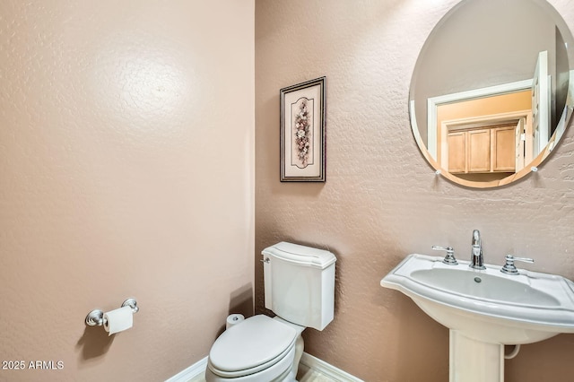 half bath with toilet, a textured wall, baseboards, and a sink