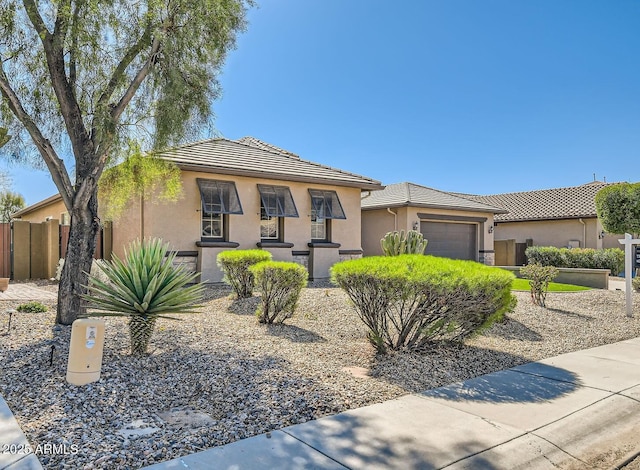 view of front of house with stucco siding, a tile roof, a garage, and fence