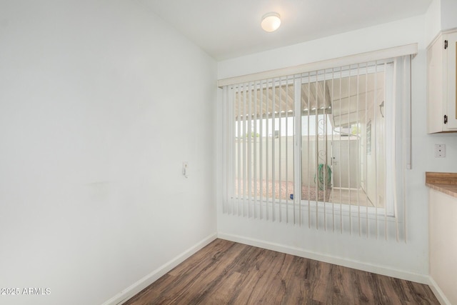 empty room featuring baseboards and dark wood finished floors