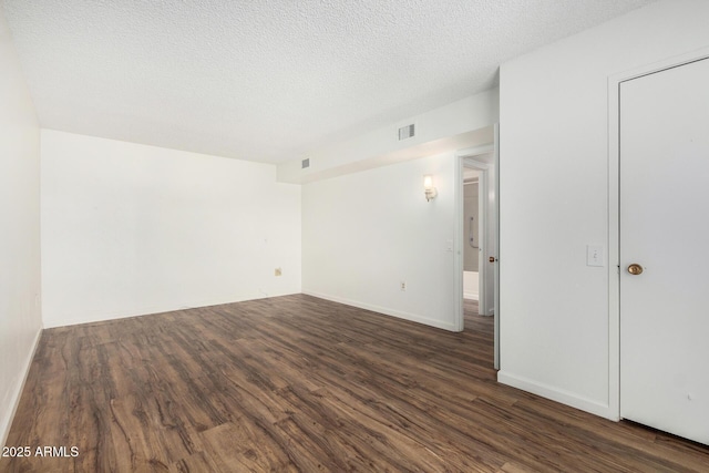 empty room featuring wood finished floors, a textured ceiling, baseboards, and visible vents