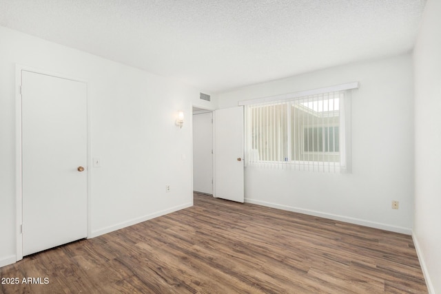 empty room featuring wood finished floors, a textured ceiling, baseboards, and visible vents