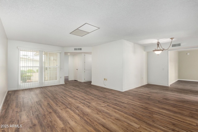 unfurnished room with a textured ceiling, visible vents, baseboards, and dark wood-style flooring