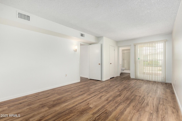spare room featuring visible vents, a textured ceiling, baseboards, and wood finished floors