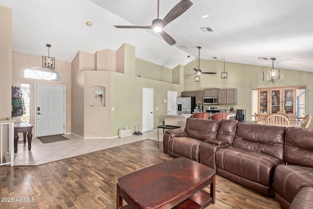 living area with light wood finished floors, visible vents, a textured ceiling, and ceiling fan with notable chandelier