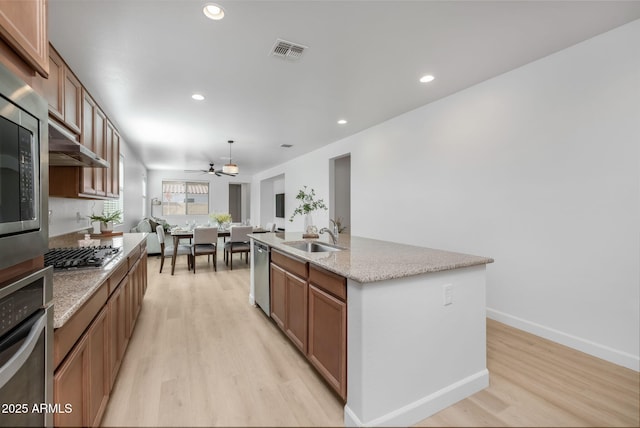 kitchen featuring decorative light fixtures, sink, stainless steel appliances, a center island with sink, and light wood-type flooring