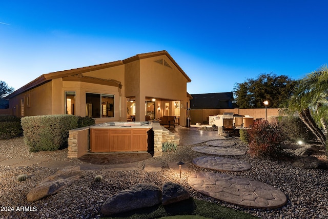 back house at dusk with an outdoor kitchen, a hot tub, and a patio area