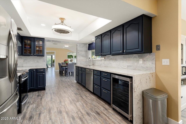 kitchen with appliances with stainless steel finishes, tasteful backsplash, wood-type flooring, a raised ceiling, and beverage cooler