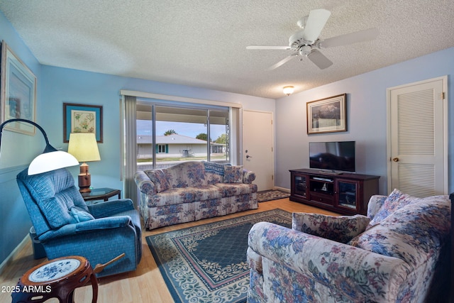 living room with a textured ceiling, ceiling fan, and light wood-type flooring