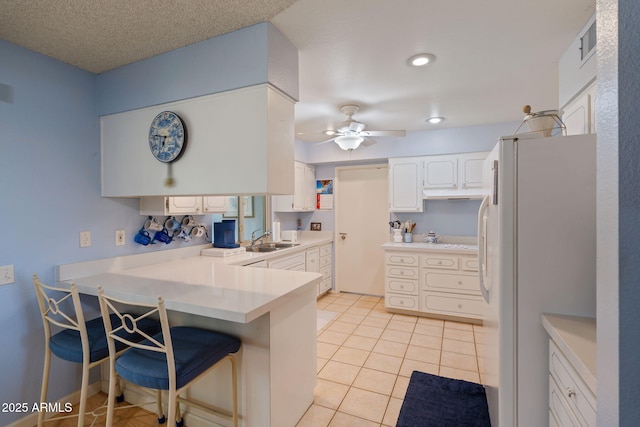 kitchen with light tile patterned floors, a breakfast bar, white cabinetry, kitchen peninsula, and white fridge