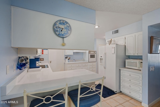 kitchen featuring white cabinetry, light tile patterned floors, a kitchen breakfast bar, kitchen peninsula, and white appliances