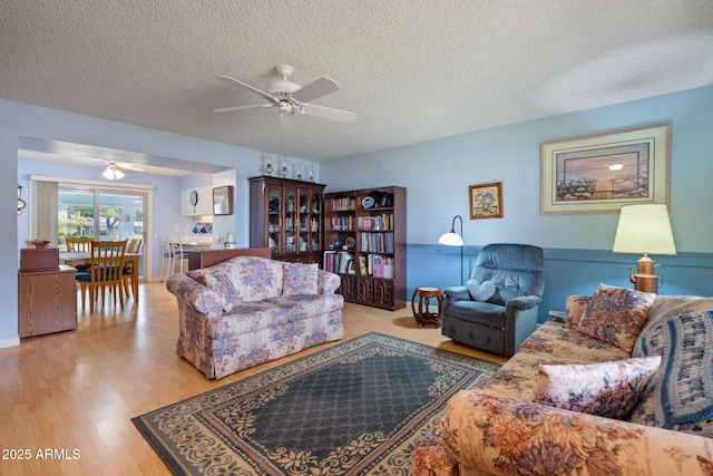 living room with ceiling fan, light hardwood / wood-style floors, and a textured ceiling