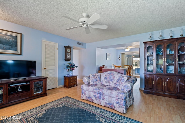 living room with ceiling fan, a textured ceiling, and light wood-type flooring