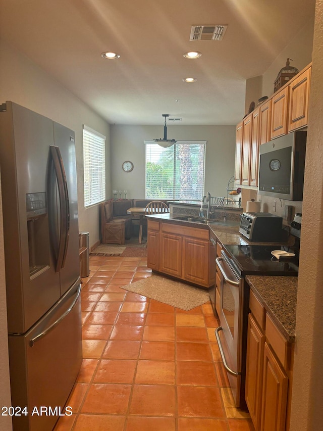 kitchen with pendant lighting, dark stone counters, sink, light tile patterned floors, and appliances with stainless steel finishes