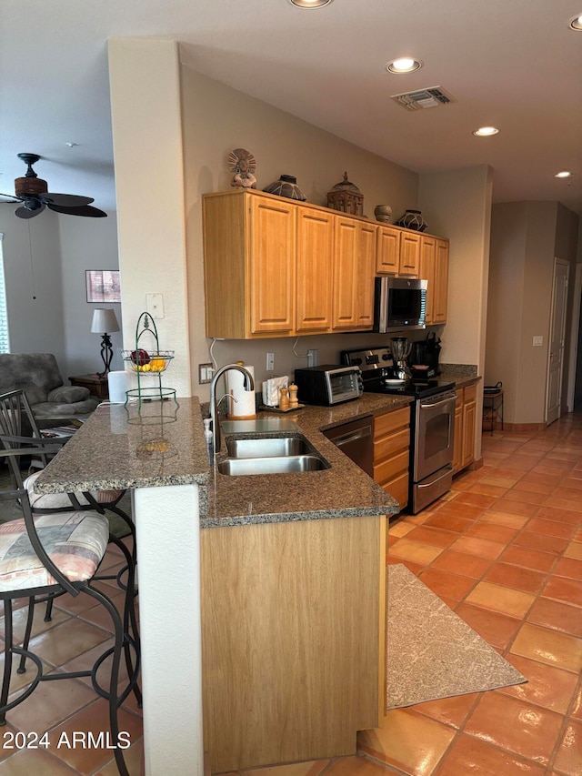 kitchen featuring kitchen peninsula, appliances with stainless steel finishes, a breakfast bar, ceiling fan, and sink