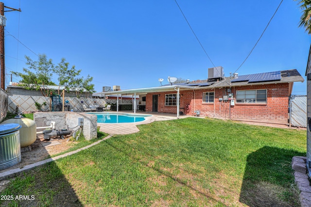 rear view of house with a patio area, brick siding, a fenced backyard, solar panels, and a lawn