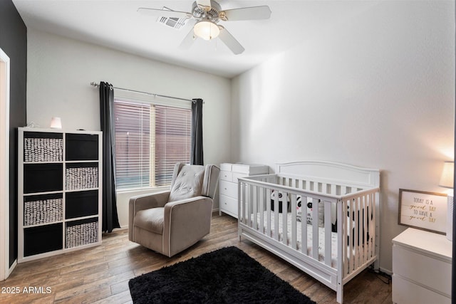 bedroom featuring a crib, hardwood / wood-style flooring, and ceiling fan