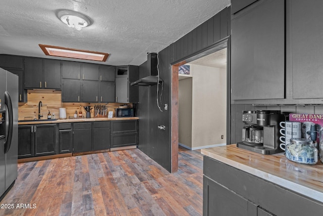 kitchen with wall chimney range hood, light countertops, a sink, and freestanding refrigerator