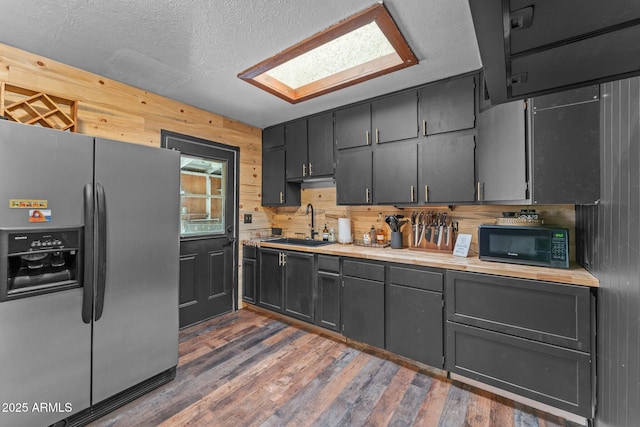 kitchen featuring light countertops, stainless steel fridge, wooden walls, a sink, and black microwave