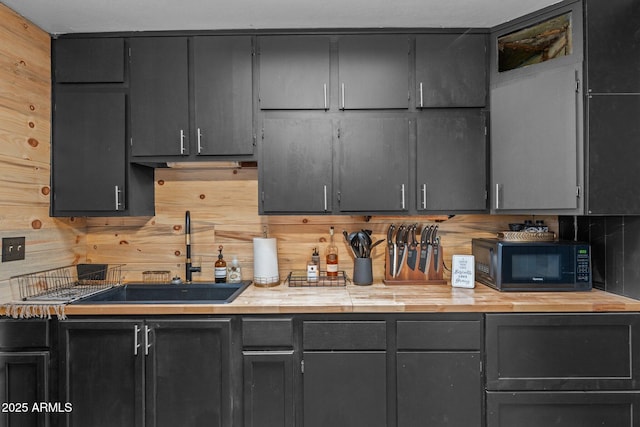 kitchen with a sink, black microwave, wood walls, wood counters, and decorative backsplash