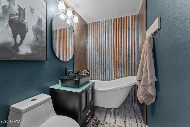 full bath featuring a textured ceiling, toilet, a freestanding tub, vanity, and a textured wall
