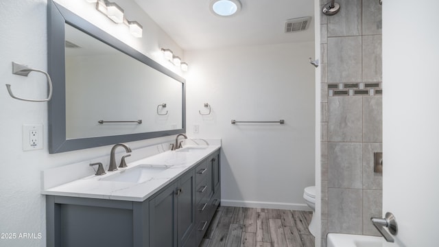 full bathroom with visible vents, baseboards, double vanity, wood finished floors, and a sink