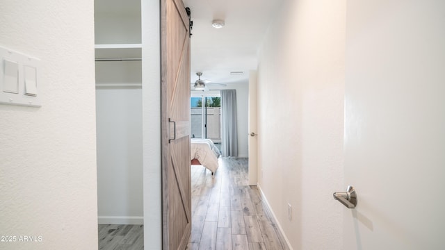 corridor with a barn door, baseboards, and light wood-style floors