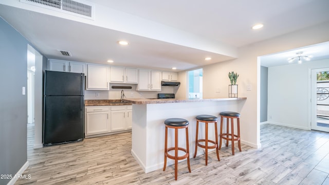 kitchen with under cabinet range hood, visible vents, light wood-style flooring, and freestanding refrigerator