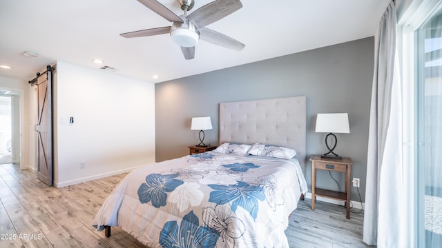 bedroom featuring a barn door, light wood-style flooring, baseboards, and visible vents