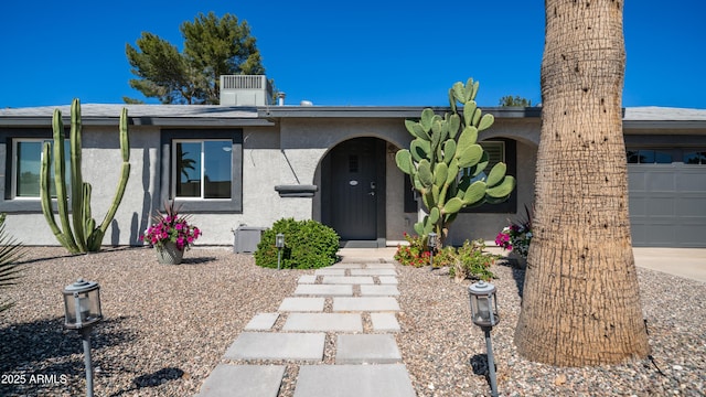 view of front of home with central AC unit, stucco siding, and an attached garage