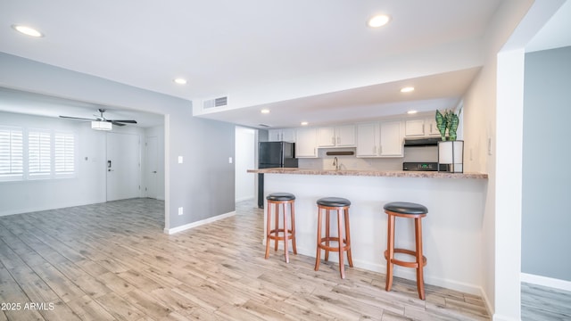 kitchen featuring a breakfast bar area, visible vents, freestanding refrigerator, white cabinets, and under cabinet range hood