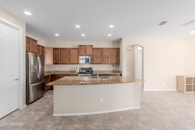 kitchen featuring stainless steel appliances, light stone countertops, sink, and a kitchen island with sink