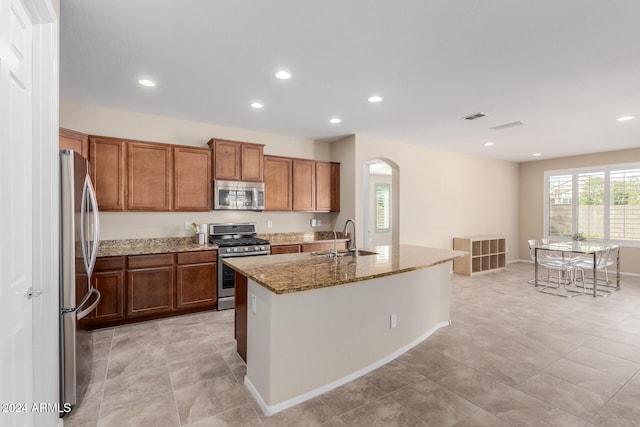 kitchen featuring sink, appliances with stainless steel finishes, light stone counters, and an island with sink