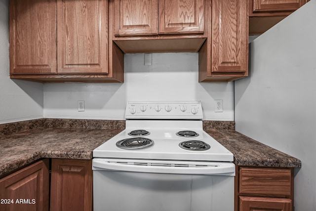 kitchen with brown cabinetry, dark countertops, and white electric range oven