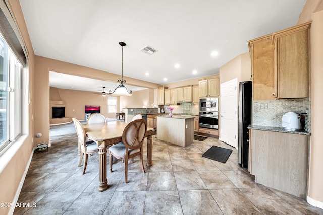 kitchen featuring appliances with stainless steel finishes, hanging light fixtures, a center island, light stone countertops, and light brown cabinets