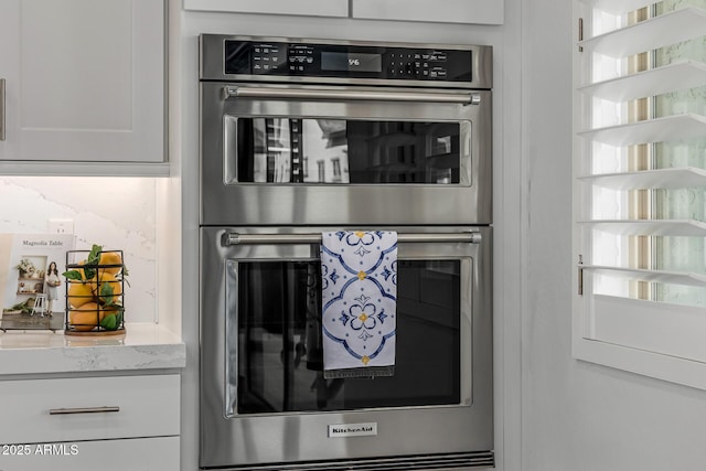 kitchen view of double oven, white cabinets, and light stone counters