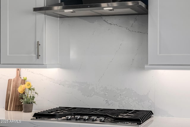 kitchen view of extractor fan, tasteful backsplash, white cabinets, and stainless steel gas stovetop