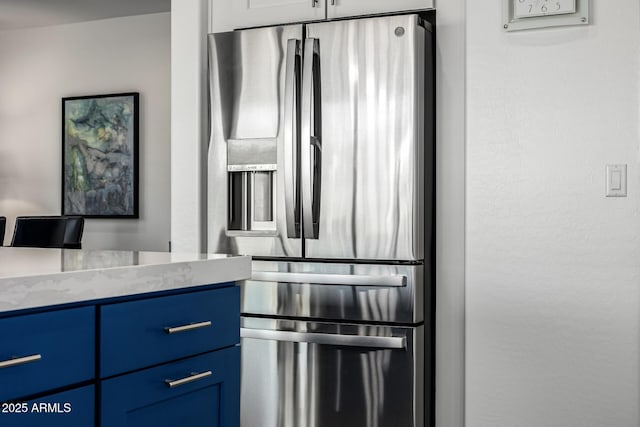 kitchen with stainless steel fridge with ice dispenser, blue cabinetry, and light stone counters