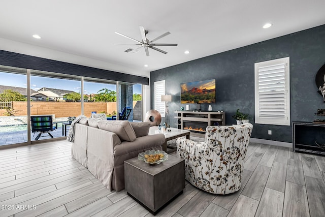 living room featuring wood finished floors, a ceiling fan, recessed lighting, a glass covered fireplace, and baseboards