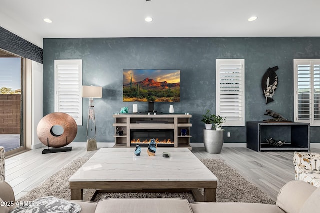living area featuring wood finished floors, a glass covered fireplace, recessed lighting, and baseboards