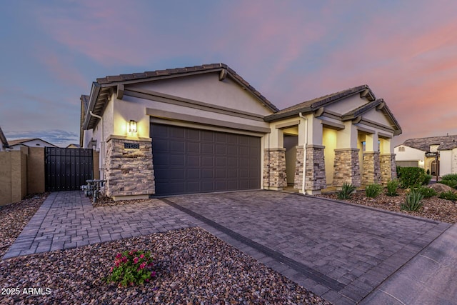 view of front facade featuring stone siding, stucco siding, a gate, decorative driveway, and an attached garage