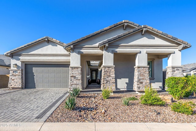 craftsman-style house featuring stucco siding, stone siding, an attached garage, and decorative driveway