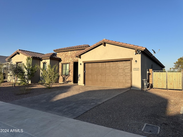 mediterranean / spanish-style home with decorative driveway, a tile roof, stucco siding, an attached garage, and stone siding