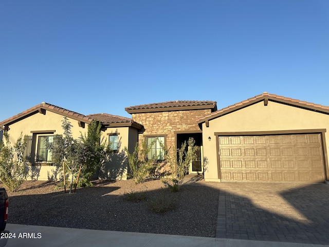 mediterranean / spanish house with stone siding, decorative driveway, an attached garage, and stucco siding