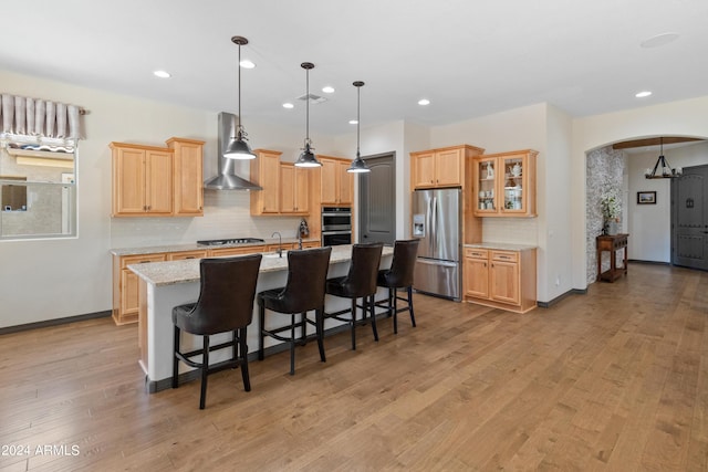 kitchen with wall chimney exhaust hood, a breakfast bar, light stone counters, a center island with sink, and stainless steel appliances