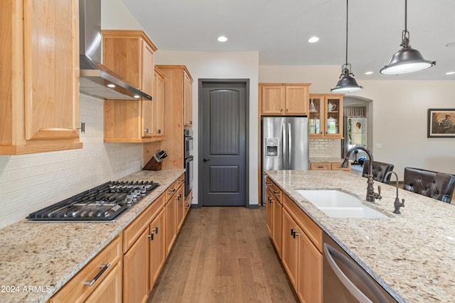 kitchen with pendant lighting, sink, light stone counters, stainless steel appliances, and wall chimney range hood