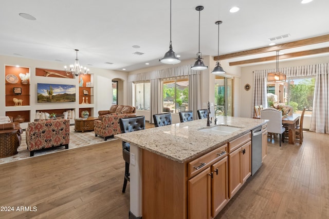 kitchen with sink, light stone counters, hanging light fixtures, dishwasher, and an island with sink