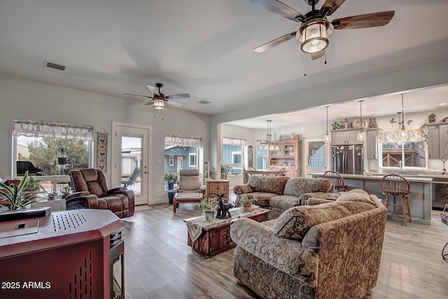 living area featuring visible vents, ceiling fan with notable chandelier, and light wood-style floors