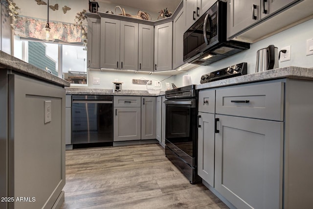 kitchen featuring gray cabinetry, light stone countertops, light wood-type flooring, black / electric stove, and stainless steel dishwasher