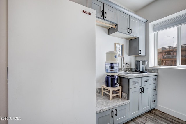 kitchen featuring wood finished floors, baseboards, gray cabinets, freestanding refrigerator, and a sink