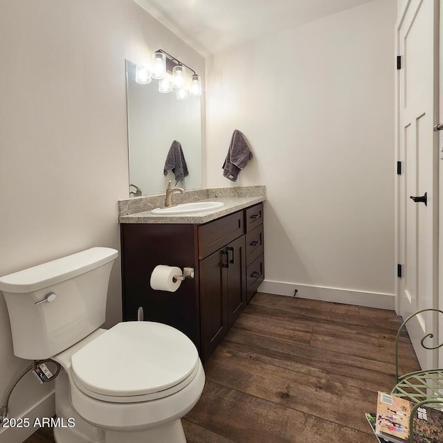 half bath with vanity, toilet, wood finished floors, and baseboards